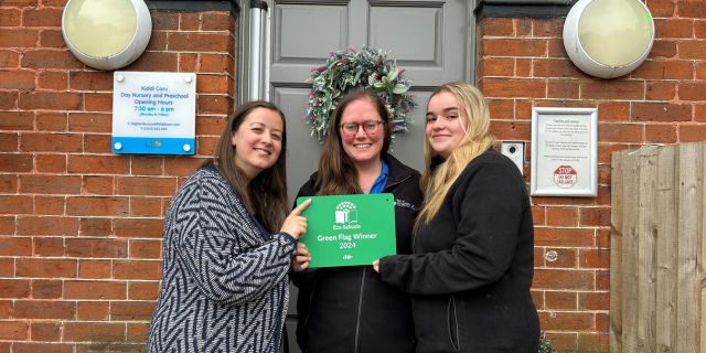 The staff team at Kiddi Caru Leighton Buzzard holding up their Eco-School plaque outside their day nursery and preschool.